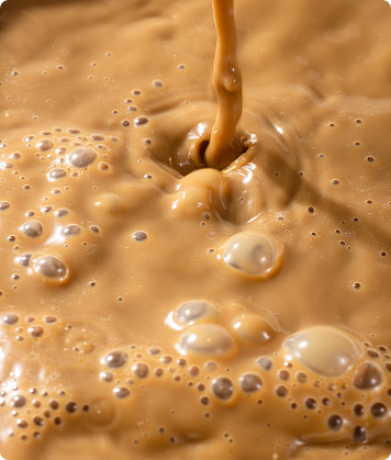 Close-up de bebida cremosa de SuperCoffee sendo despejada, com espuma e bolhas na superfície.