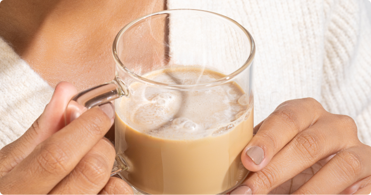 Pessoa segurando um copo transparente com SuperCoffee cremoso, em close-up.